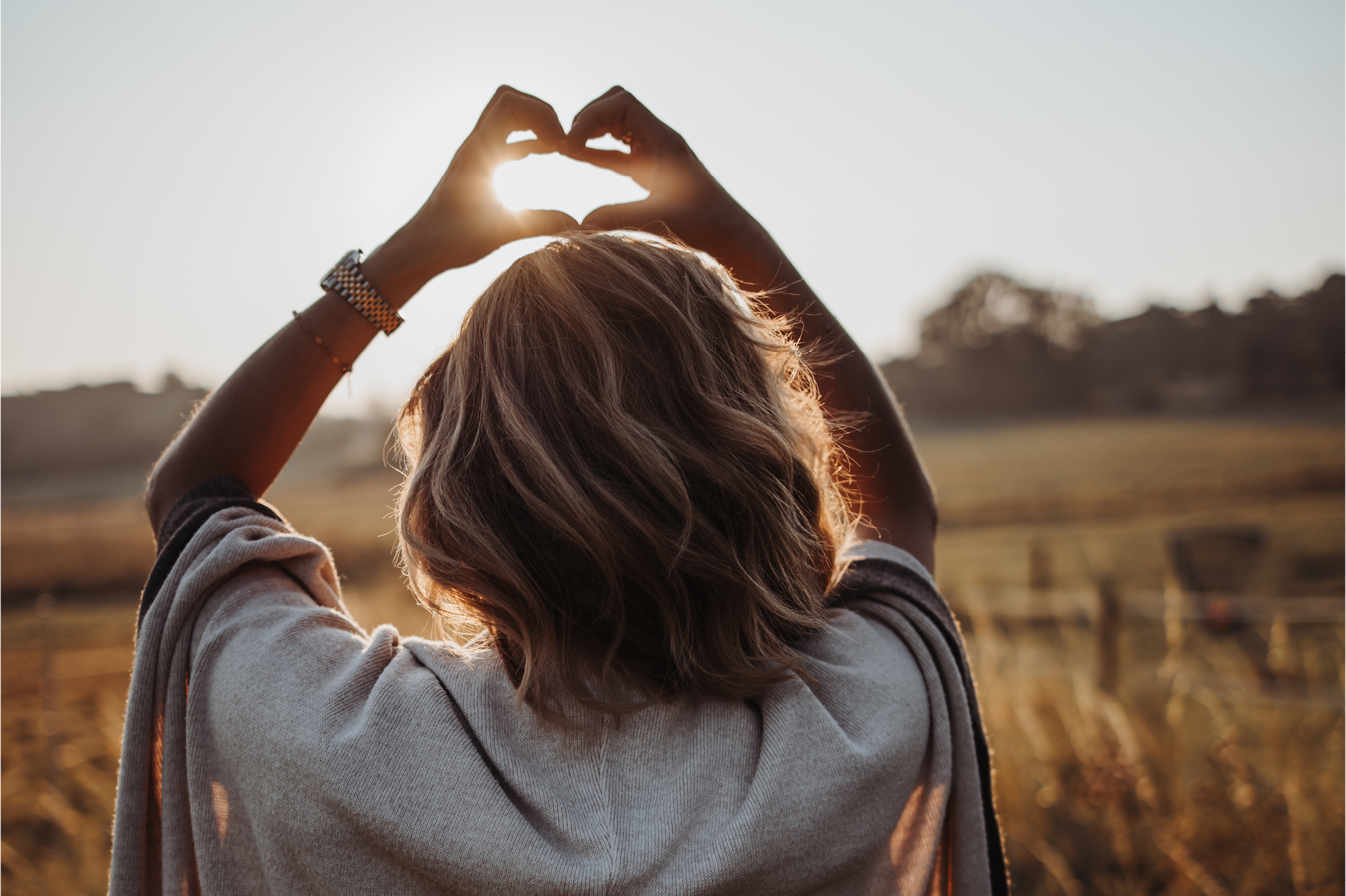Headerbild Frau die ein Herz mit den Händen um die Sonne formt im Abendsonnenlicht